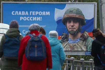 People at a tram stop in front of a board displaying a portrait of a Russian soldier in Saint Petersburg on Wednesday.