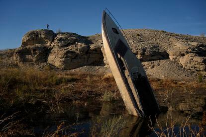 A man stands on a hill overlooking a formerly sunken boat standing upright into the air with its stern buried in the mud along the shoreline of Lake Mead at the Lake Mead National Recreation Area, Friday, Jan. 27, 2023, near Boulder City, Nev.