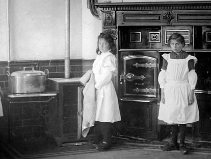 Two girls pose in the kitchen of the house where they worked as maids, in an image dated to the Victorian era.