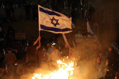 Protesters block a road and hold national flags as they gather around a bonfire during a rally against the Israeli government's judicial reform in Tel Aviv, Israel on March 27, 2023.