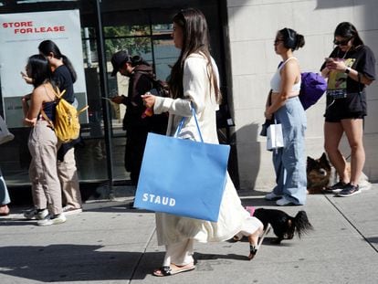 A woman carrying a shopping bag walks past people queuing for a pop-up shop in the SoHo neighborhood of New York City, September 21, 2023.