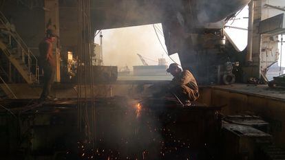 A worker uses a torch to cut through steel on a ship.