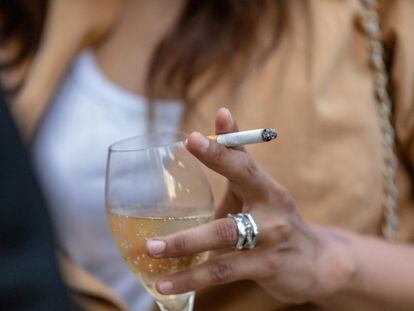 A woman smokes a cigarrette while having a drink.