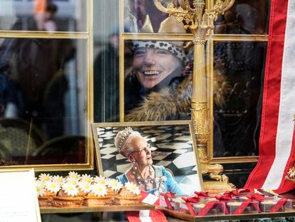 A woman wearing a crown smiles behind a window of a cafe where a picture of Danish Queen Margrethe is on display in Copenhagen, Denmark, Sunday, Jan. 14, 2024.