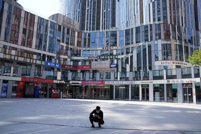 A man wearing a mask squats in front of an empty mall area in Beijing. 