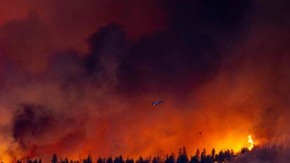 A helicopter battles the McDougall Creek wildfire as it burns in the hills West Kelowna, British Columbia, Canada, on August 17, 2023, as seen from Kelowna.