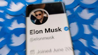 Elon Musk's profile on Twitter, displayed on a mobile phone over logos of the social network.