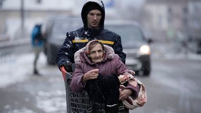 An elderly woman is carried to safety inside a shopping cart in the Ukrainian city of Irpin, which is under attack.