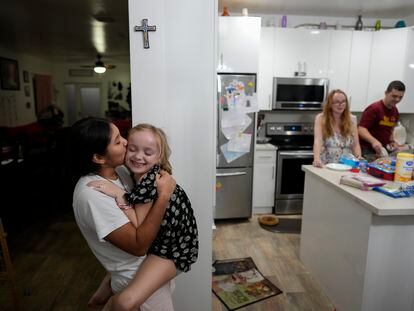 Sol, left, a 14-year-old from Argentina, kisses 8-year-old Maddie Hazelton as they play together in the kitchen of Sol's foster parents, Andy, right, and Caroline Hazelton, in Homestead, Fla., Monday, Dec. 18, 2023.