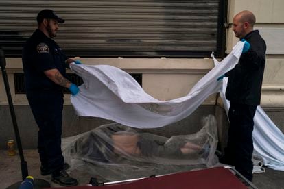 Forensic assistant Laurentiu Bigu, left, and investigator Ryan Parraz from the Los Angeles County coroner's office cover the body of a homeless man